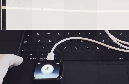 A finger holds down the button on the TapTalk device; it glows, then releases, and the words 'Hello, world.' are typed into the document on the connected iPad.